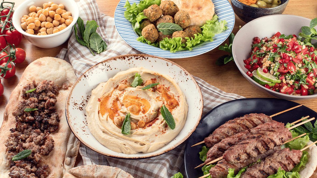 Homemade hummus with olive oil and paprika, pita, kebabs and salads on a table